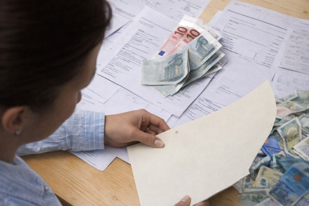 En kvinde gennemgår papirer og eurosedler ved et bord.